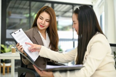 Çekici Asyalı iş kadını, meslektaşının raporla ilgili tavsiyelerini dinlemeye, iş görüşmelerine ve ofiste birlikte çalışmaya odaklanıyor..