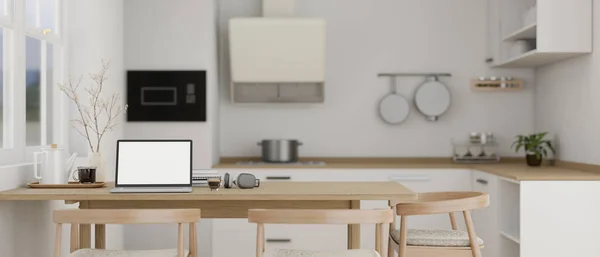 stock image A laptop computer white screen mockup on a wooden dining table in modern contemporary white kitchen with kitchen appliances. 3d render, 3d illustration