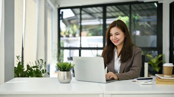 Attractive and gorgeous millennial Asian businesswoman or female manager using her laptop computer at her desk in her private office.