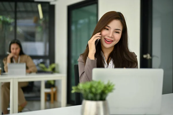 彼女のオフィスに座っている間 彼女のクライアントに電話で専門的なアドバイスを与える魅力的で笑顔のミレニアル世代アジアのビジネス女性や女性保険代理店 — ストック写真