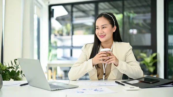 笑顔と幸せな千年のアジアのビジネスマンの女性は窓の外を見て 彼女の机で朝のコーヒーを飲みながら彼女のキャリアの成功を夢見て — ストック写真