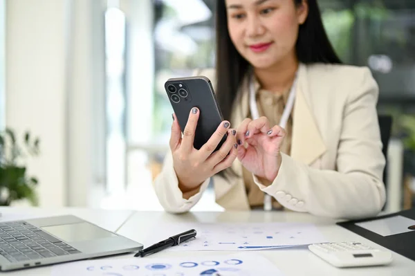 stock image Close-up image of a professional millennial Asian businesswoman or female accountant sending message to someone on her phone, using her smartphone at her desk.