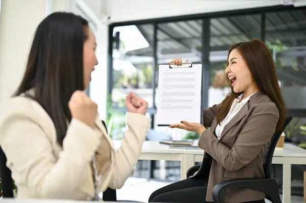 2人の興奮し 喜びに満ちた若いアジアのビジネスマンの女性は 書類を見て 仕事の昇進やプロジェクトが承認され 彼らのオフィスで祝う — ストック写真