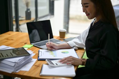 Masasında hesap makinesi kullanan ve mali raporları analiz eden Asyalı profesyonel ve güzel bir iş kadını ya da kadın finans asistanının yakın plan görüntüsü..
