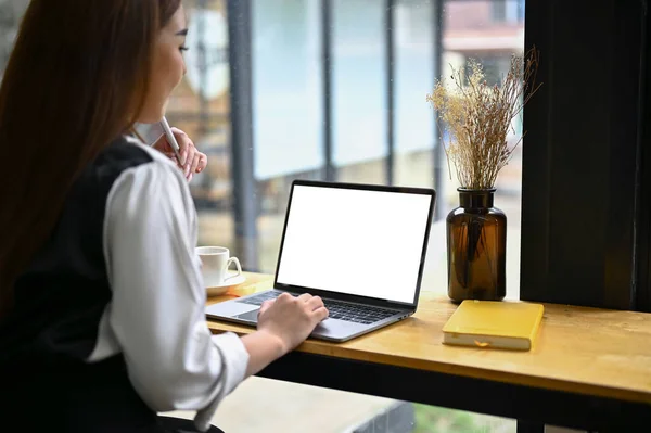 Close-up image of a beautiful Asian female office worker, remote working and using her portable laptop in a coffee shop. laptop white screen mockup