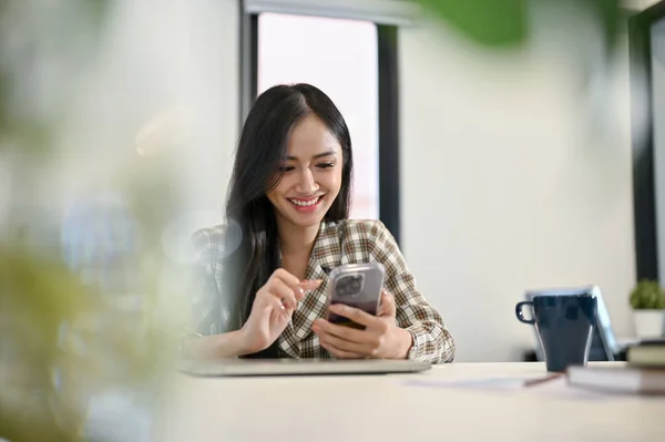 年轻的亚洲女办公室职员坐在办公室里 一边用智能手机笑一边笑 — 图库照片