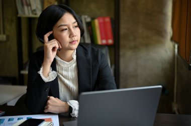 Bin yıllık düşünceli Asyalı iş kadını ya da kadın yönetici. Düşünceli, düşünen bir yüzle pencereden dışarı bakıyor. Yeni iş projesi için endişeleniyor, sorunları çözüyor..