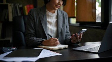 Bin yıllık Asyalı profesyonel bir iş kadını ya da kadın patronun internetten bilgi arama ve masasındaki not defterine not alma görüntüleri..