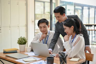 Profesyonel ve zeki bir Asyalı erkek patron işi tartışıyor, tavsiyelerde bulunuyor ve ofisteki bir dizüstü bilgisayardan çalışanlarının yeni projesini kontrol ediyor..