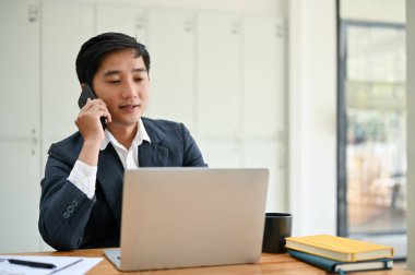 Profesyonel bir Asyalı işadamı telefonda masasında otururken iş müşterisine danışmanlık yapıyor..