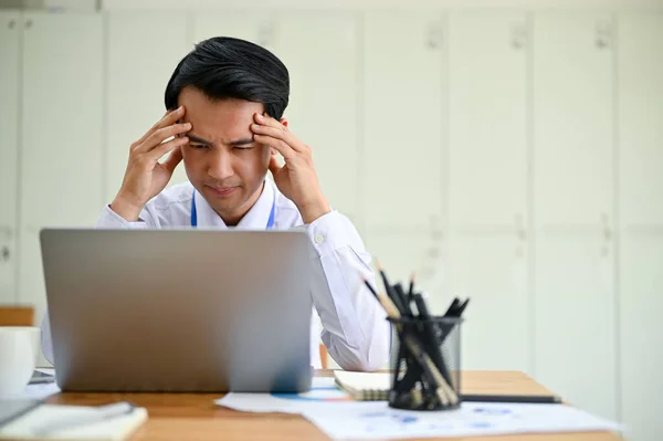 stock image Stressed and serious Asian male office worker worried about a project's deadline, having trouble with the financial data on his computer. Overwork, Headache, Unhappy