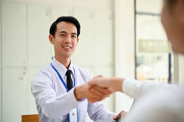 一位英俊而快乐的千年亚洲商人在办公室里握手欢迎客人 — 图库照片