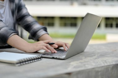 İnternette bilgi arayan bir üniversite öğrencisinin üniversite parkındaki dizüstü bilgisayarını kullanarak yakın plan görüntüsü..