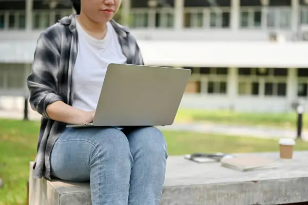 一名身穿休闲装的年轻亚洲女大学生在校园公园的长椅上使用手提电脑的剪影 — 图库照片