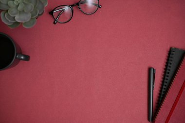 Çalışma alanı üst görünümü gözlük, kalem, kitap, kahve fincanı, saksı bitkisi ve kırmızı arka planda ürününüz veya metin gösteriminiz için kopya alanı.