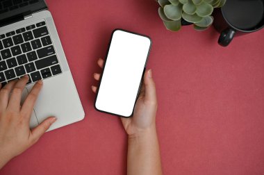 Yaratıcı kırmızı masasında akıllı telefonunu ve dizüstü bilgisayarını kullanan bir iş kadınının en iyi görüntüsü. akıllı telefon beyaz ekran modeli