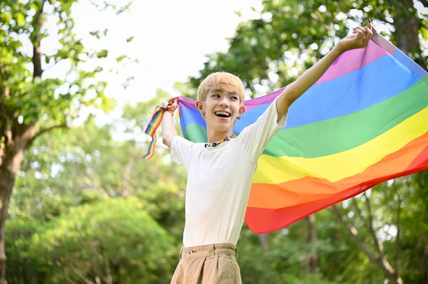 一位年轻迷人而快乐的亚洲同性恋男子的画像 他身披Lgbt彩虹旗 站在绿色的公园里 感到自由和自豪 — 图库照片