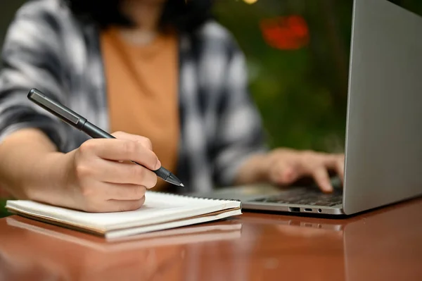 stock image Cropped image of a young Asian female college student or a freelancer working on her tasks on laptop at an outdoor cafe.