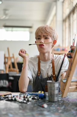 Yaratıcı ve çekici Asyalı eşcinsel eşcinsel bir sanatçının portresi yaratıcı sanat atölyesinin keyfini çıkarıyor, stüdyodaki yaratıcı atölyesinde tuvalin önünde oturuyor..