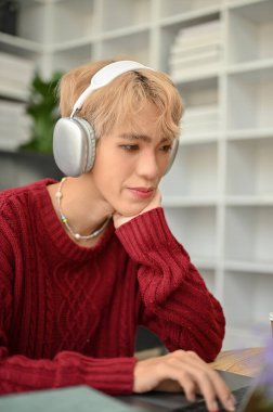 Çekici Asyalı genç eşcinsel bir adamın portresi dizüstü bilgisayarına odaklanıyor ya da oturma odasında otururken bir web sitesinde bir şeyler okuyor..