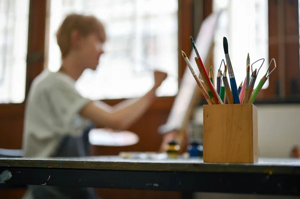 在一个模糊的画布上的人的背景上 一个铅笔架和各种铅笔和绘画工具在桌子上的特写图像 选择性聚焦图像 — 图库照片