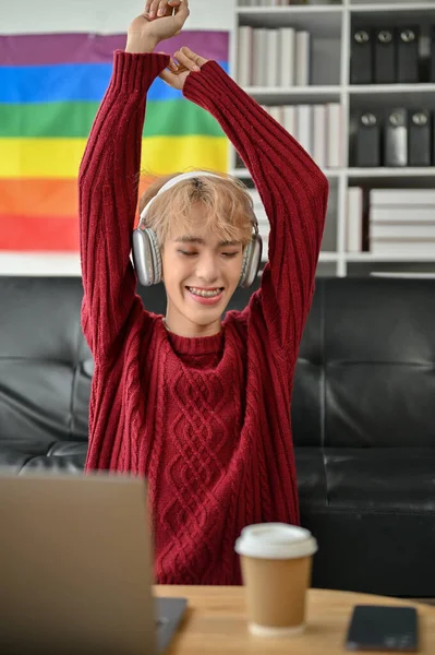 一位快乐的亚洲同性恋年轻人正坐在客厅的沙发上 一边用耳机欣赏音乐 一边跳舞 生活方式概念 — 图库照片