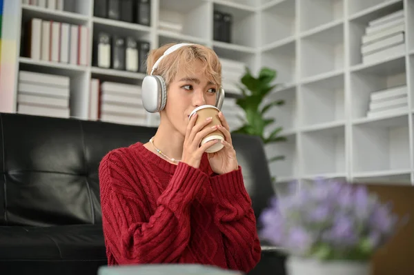 매력적 아시아 헤드폰을 거실에서 커피를 마시며 음악을 즐기고 — 스톡 사진