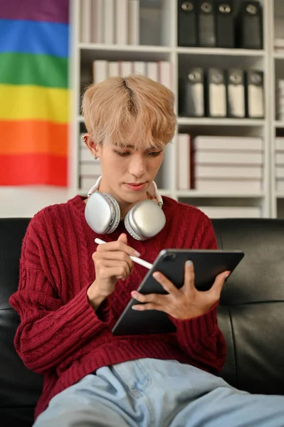 在客厅的沙发上 一个身穿休闲装的年轻貌美的亚洲同性恋男子的肖像被放在了他的平板电脑屏幕上 — 图库照片