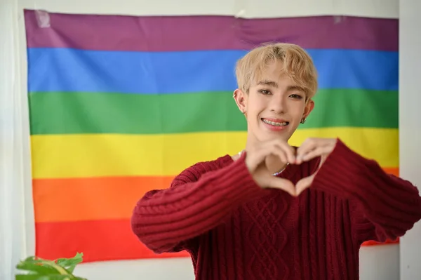 一位笑着的年轻亚洲同性恋者或同性恋男子站在房间里时 在墙上挂着一面Lgbt彩虹旗 展示了他的心迹 Lgbtq — 图库照片