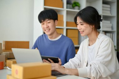 Genç ve güzel Asyalı bir bayan çevrimiçi dükkan sahibi erkek arkadaşıyla bilgisayardaki ürün stoklarını konuşuyor ve kontrol ediyor..