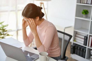 Modern bir ofiste masasında çalışan stresli ve ciddi Asyalı iş kadını, projenin bitiş tarihinden veya işiyle ilgili sorunları olmasından endişe ediyor..