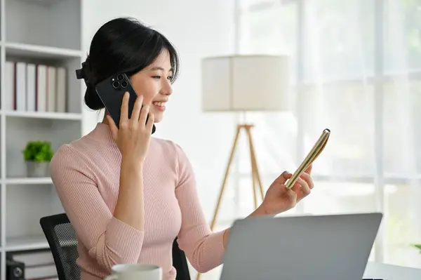 Gyönyörű Sikeres Ázsiai Üzletasszony Nézi Részleteket Egy Jegyzetfüzetben Miközben Telefonon — Stock Fotó