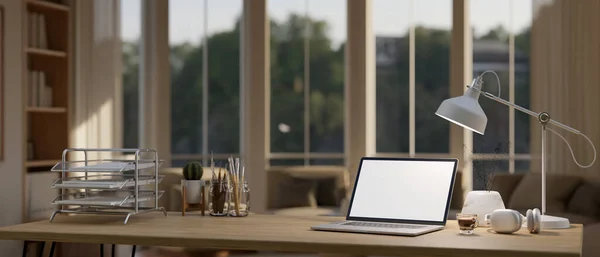 stock image A laptop white screen mockup, table lamp, headphones, stationery and office supplies on a wooden tabletop in a beautiful cozy private office. 3d render, 3d illustration