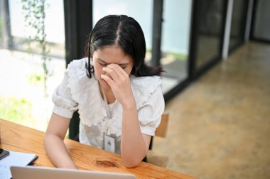 Uzun bir iş gününden sonra baş ağrısı çeken Asyalı genç ve yorgun ofis çalışanı. Aşırı çalışma, depresyon, üzüntü, hüsran