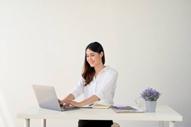Çekici genç Asyalı iş kadını ya da ofis çalışanı. Masasında beyaz duvarlı bir odada bilgisayarını kullanıyor..