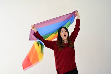 Gökkuşağı renkli LGBT bayrağı taşıyan neşeli ve neşeli Asyalı bir kadın izole edilmiş beyaz bir stüdyo arka planının üzerinde duruyor. LGBTQ + gurur ayı, lezbiyen, biseksüel