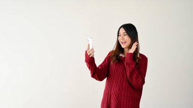 Samimi kırmızı kazaklı neşeli ve pozitif Asyalı bir kadın arkadaşıyla video görüşmesinde konuşmaktan zevk alır, elini sallayarak selam verir ya da güle güle der. beyaz arkaplanda izole
