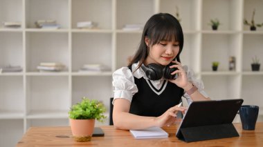 Gayri resmi giyinen genç Asyalı bir kadın, kafeteryada otururken dijital tablet kullanıyor..