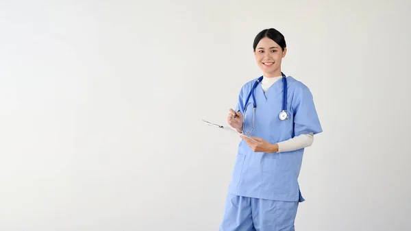 魅力的で魅力的な若いアジアの女性医師や医療従事者は 孤立した白い背景を背景に立っている間 医療用クリップボードを保持しています テキストを表示するためのコピースペース — ストック写真