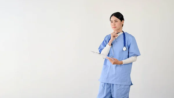 専門的かつ賢明な若いアジアの女性医師が医療用クリップボードを保持しており 治療計画について考えています 隔離された白い背景にスペースをコピーし — ストック写真