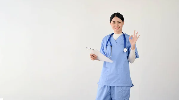 女医生亚洲一位专业而漂亮的年轻女医生或女医务工作者 穿着洗涤剂 手部有 字的签名 手持医疗剪贴板被白色背景隔离 干得好 太棒了 — 图库照片