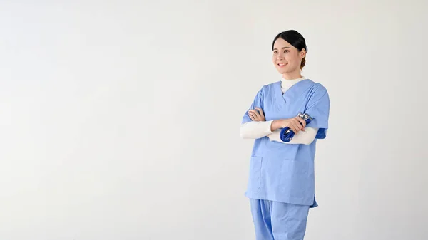 一位有魅力的 积极的亚洲年轻女医生或女医务工作者正把目光投向旁边的复制空间 她双臂交叉地站在一个孤立的白色背景下 医务工作者概念 — 图库照片