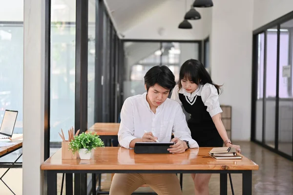 stock image A professional and smart millennial Asian male office worker is working on a project with his colleague in the office. Teamwork concept