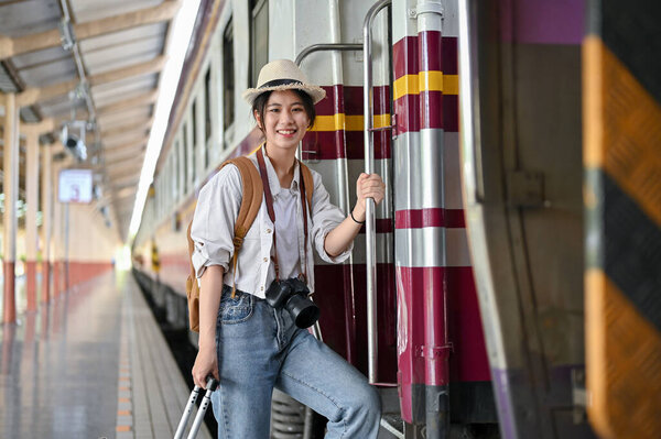 A beautiful and positive young Asian female traveler backpacker is boarding the train at the railway station. Summer vacation, Solo travel, Holidays