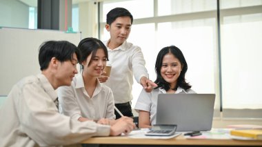 Zeki ve profesyonel bir yetişkin Asyalı işadamı veya erkek patron, genç çalışanlarına ofiste yeni bir projede koçluk yapıyor ve brifing veriyor. Takım çalışması konsepti