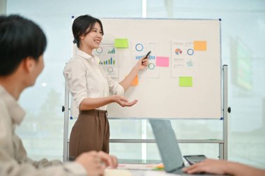 Güvenilir ve profesyonel bir Asyalı iş kadını veya kadın finans analisti toplantıda ekibine bir mali grafik ve çizelge sunuyor..