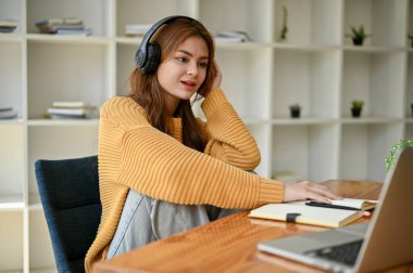 Rahat ve rahat bir Asyalı kadın oturma odasındaki masada ödev yaparken kulaklıkla müzik dinliyor..