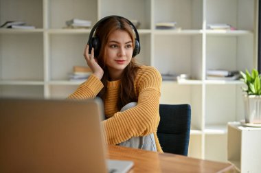 Rahat ve güzel Asyalı bir kadın rahat bir kazakla kulaklıklarıyla müzik dinliyor, hayal kuruyor ve kahve dükkanının içindeki masada otururken pencereden dışarı bakıyor..