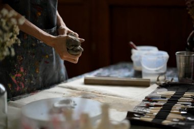 Close-up image of a master clay artist or potter kneading raw clay at his desk in the creative dark studio. clipart