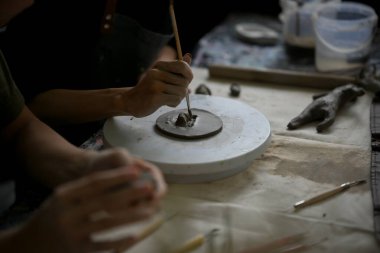 Yaratıcı ve yetenekli bir erkek çömlek sanatçısının yakın plan görüntüsü. Elinde sopa, işlenmemiş kil üzerinde desenler yapıyor, yaratıcı stüdyosunda çalışıyor..